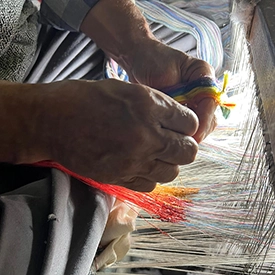 weaver tying coloured threads on a traditional loom