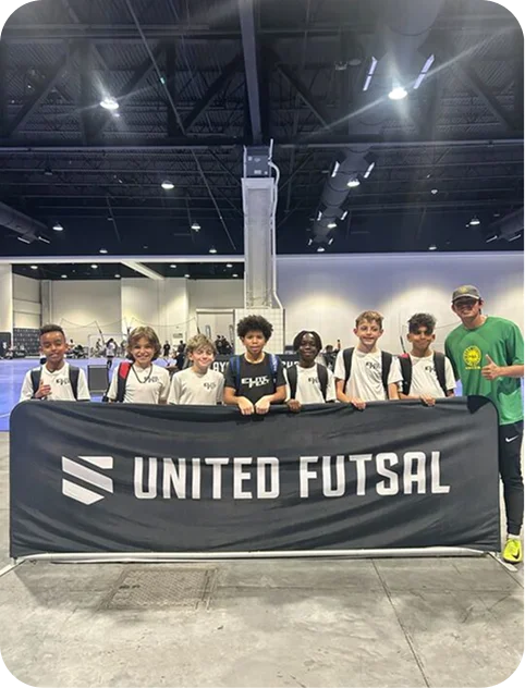 Seven young boys and one man standing indoors behind a black banner that reads 'UNITED FUTSAL'.
