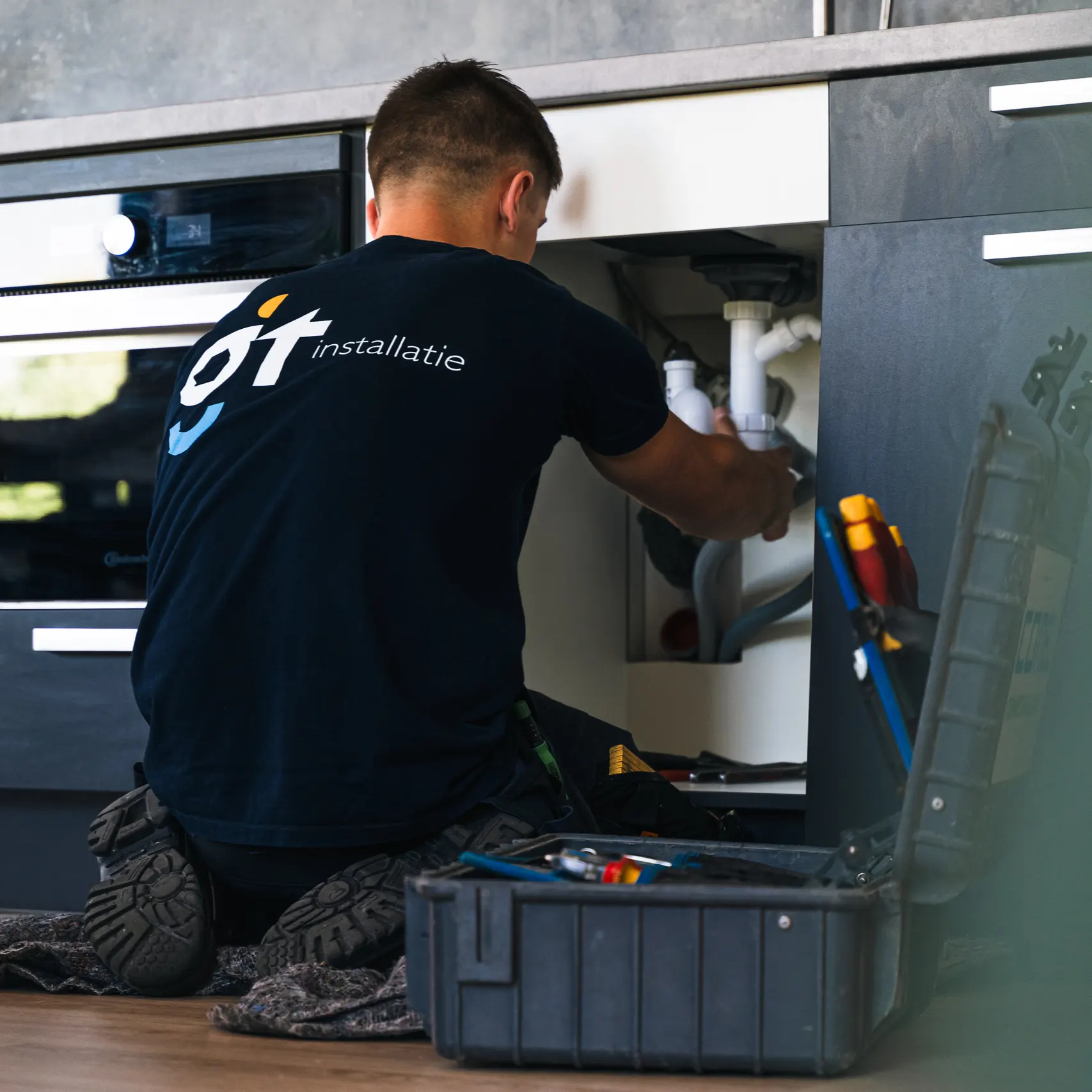 Installatiemonteur voert onderhoud uit aan leidingen en afvoer onder keukenkastje tijdens service en onderhoud.