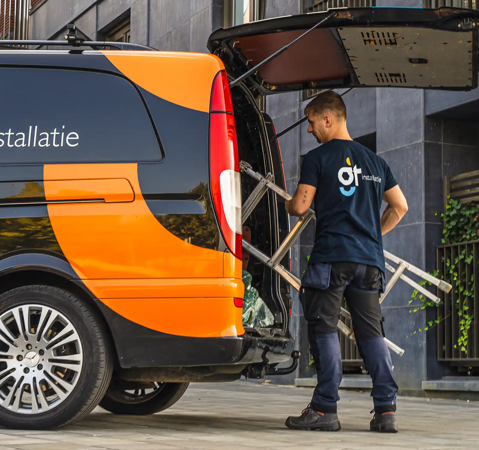 Installatiemonteur laadt materiaal uit servicebus voor installatie van technische installaties bij een gebouw.