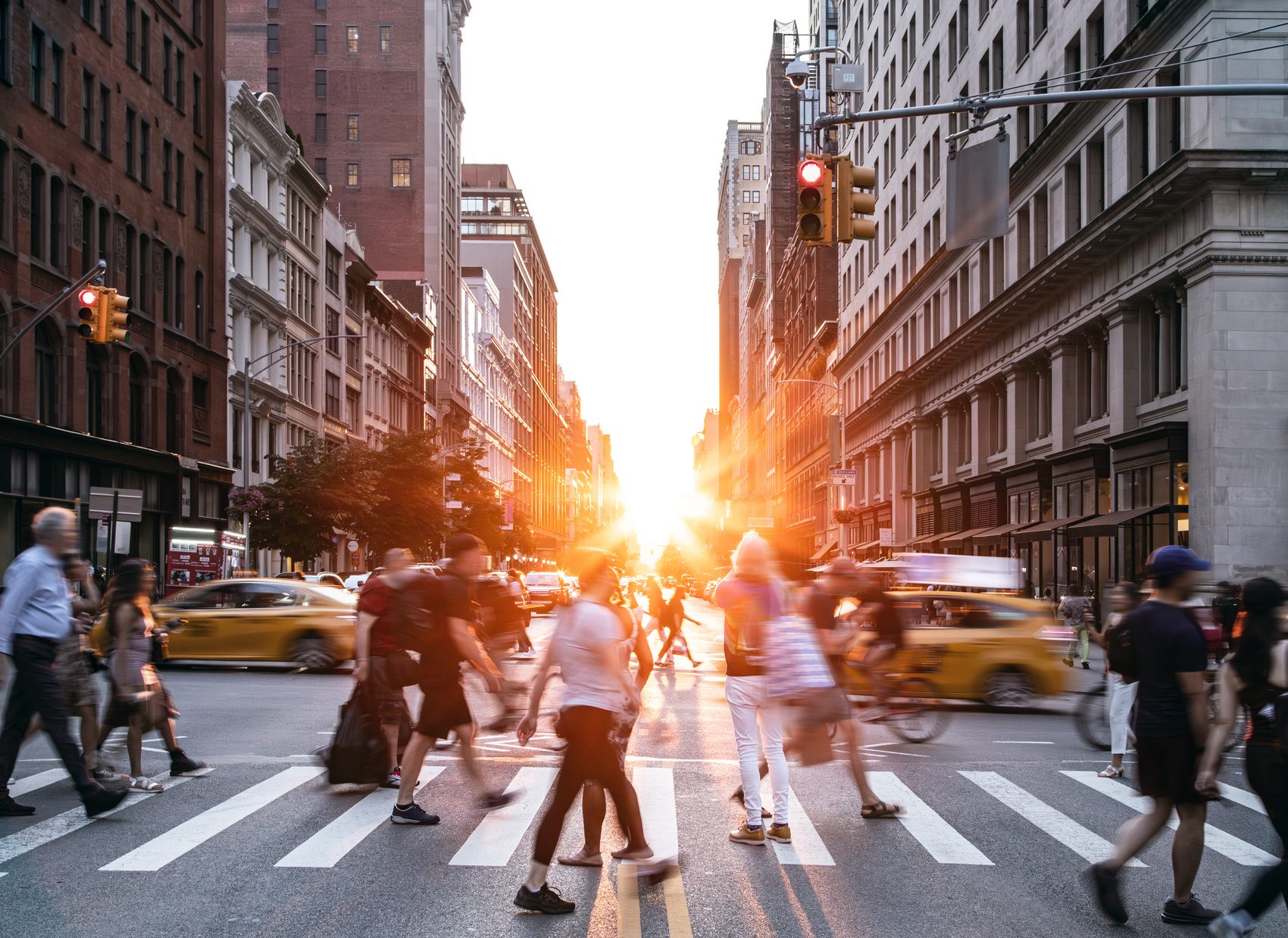 Pedestrians crossing a busy city street at sunset