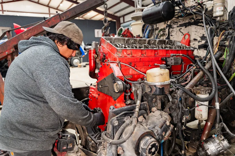 Mechanic performing engine overhaul on a large red diesel block surrounded by hoses and wiring.