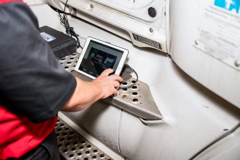 Technician uses diagnostic tablet to troubleshoot electrical problems on a heavy-duty truck step panel.