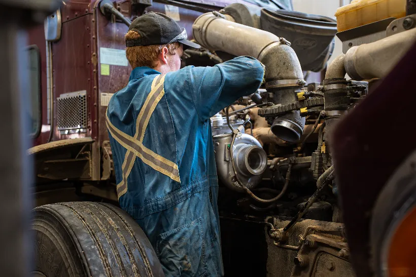 Mechanic performing an engine overhaul on a semi-truck, with turbo and intake piping exposed.