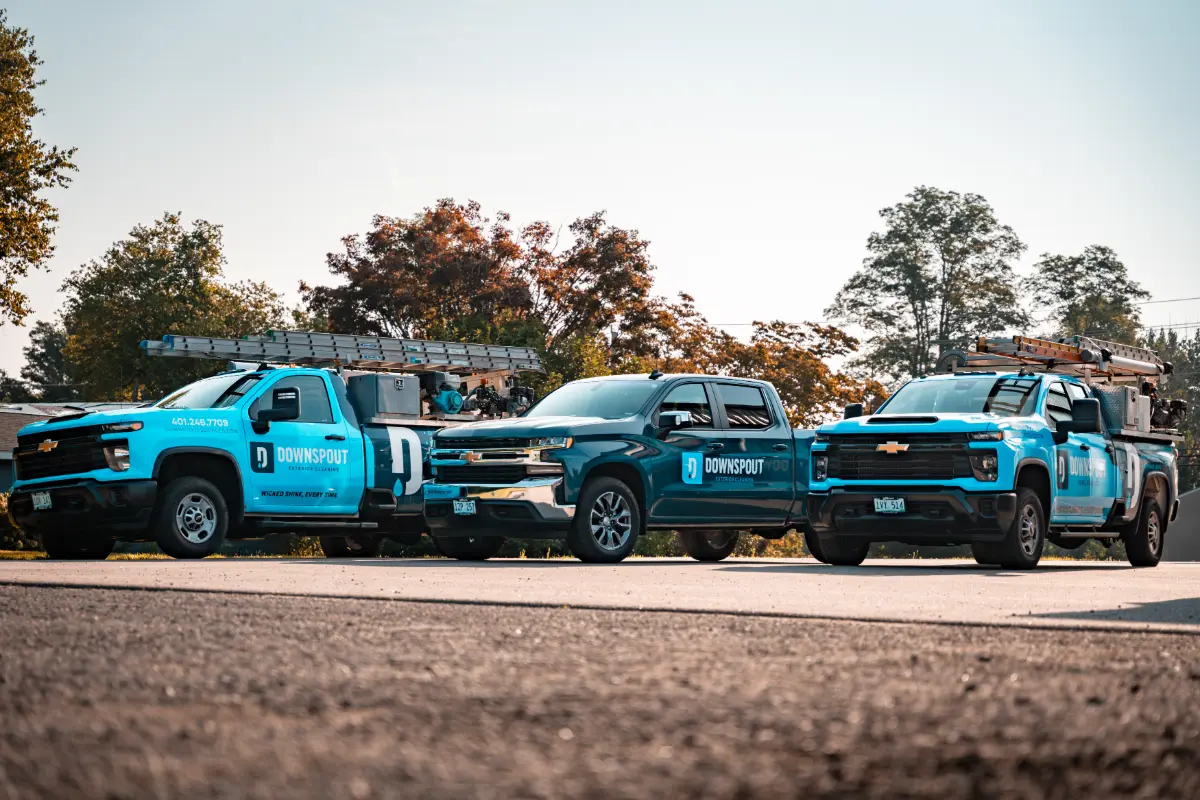 Three blue Downspout company trucks parked side by side with ladders on top during daytime.
