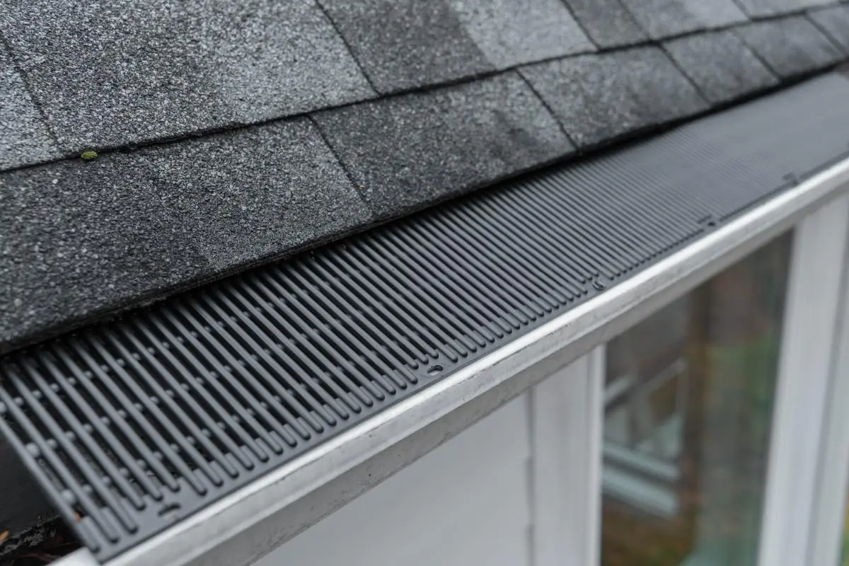 Close-up of a roof edge showing asphalt shingles and a black gutter guard covering the rain gutter.