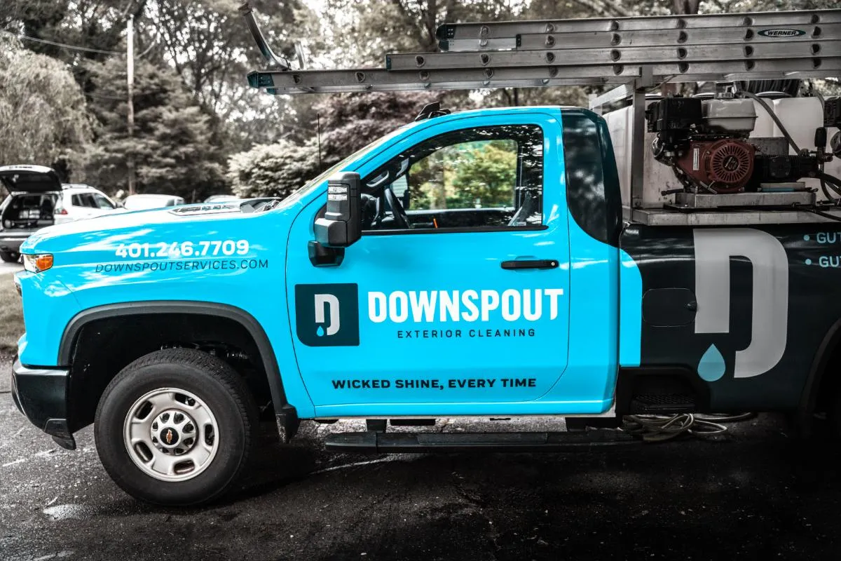 Blue and black Downspout exterior cleaning service truck with ladder on top, phone number and slogan 'Wicked Shine, Every Time' on the door.
