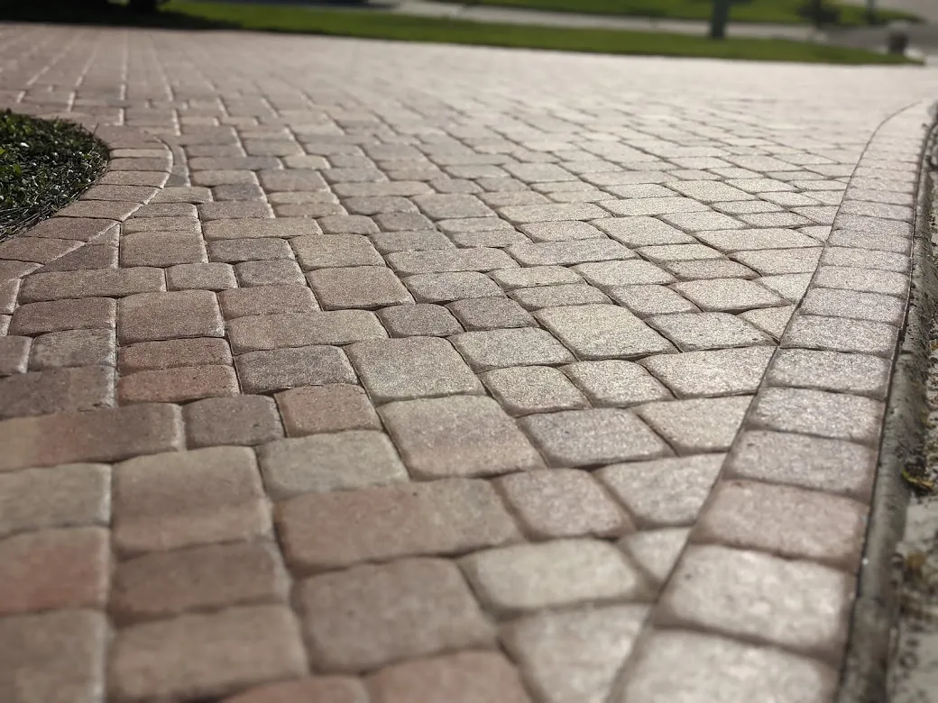 Close-up of a paved driveway with interlocking stone bricks in a beige and light brown pattern.
