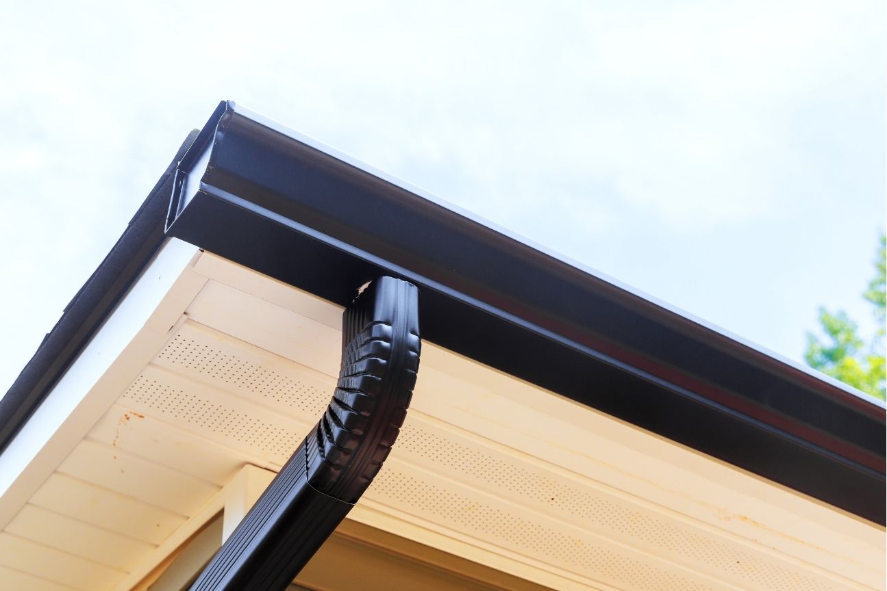 Black seamless gutters with downspout installed on residential soffit with vented panels
