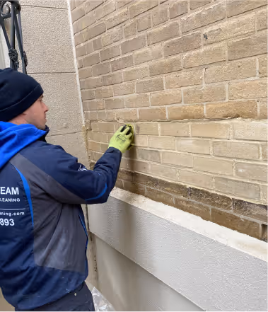 Worker in blue uniform cleaning a brick wall with a sponge cloth wearing green gloves.