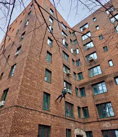 Worker suspended by ropes cleaning or repairing windows on a tall brick apartment building.