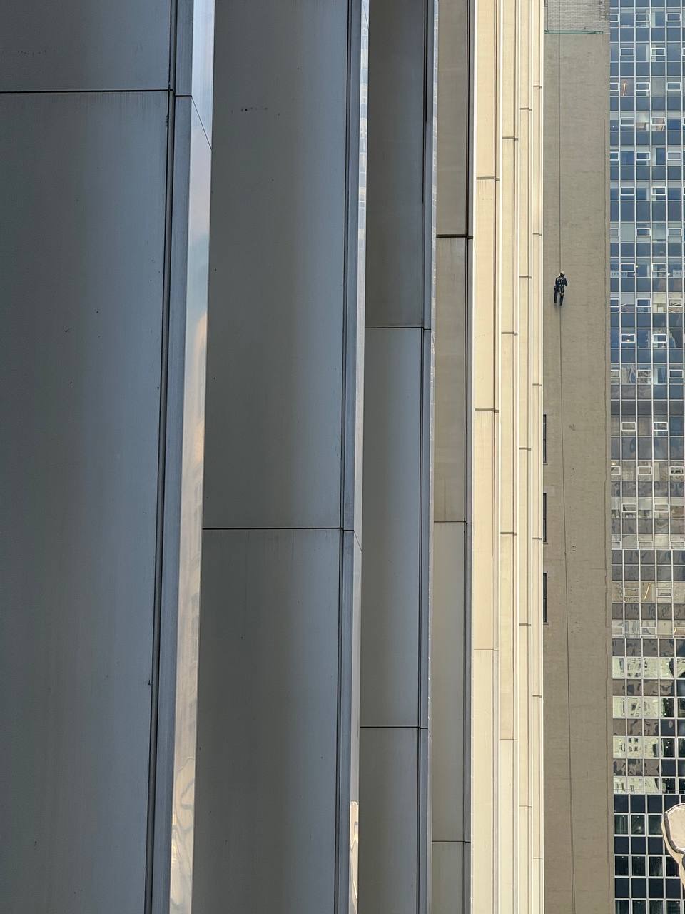 A person in climbing gear rappelling down the side of a tall building with vertical columns and windows.