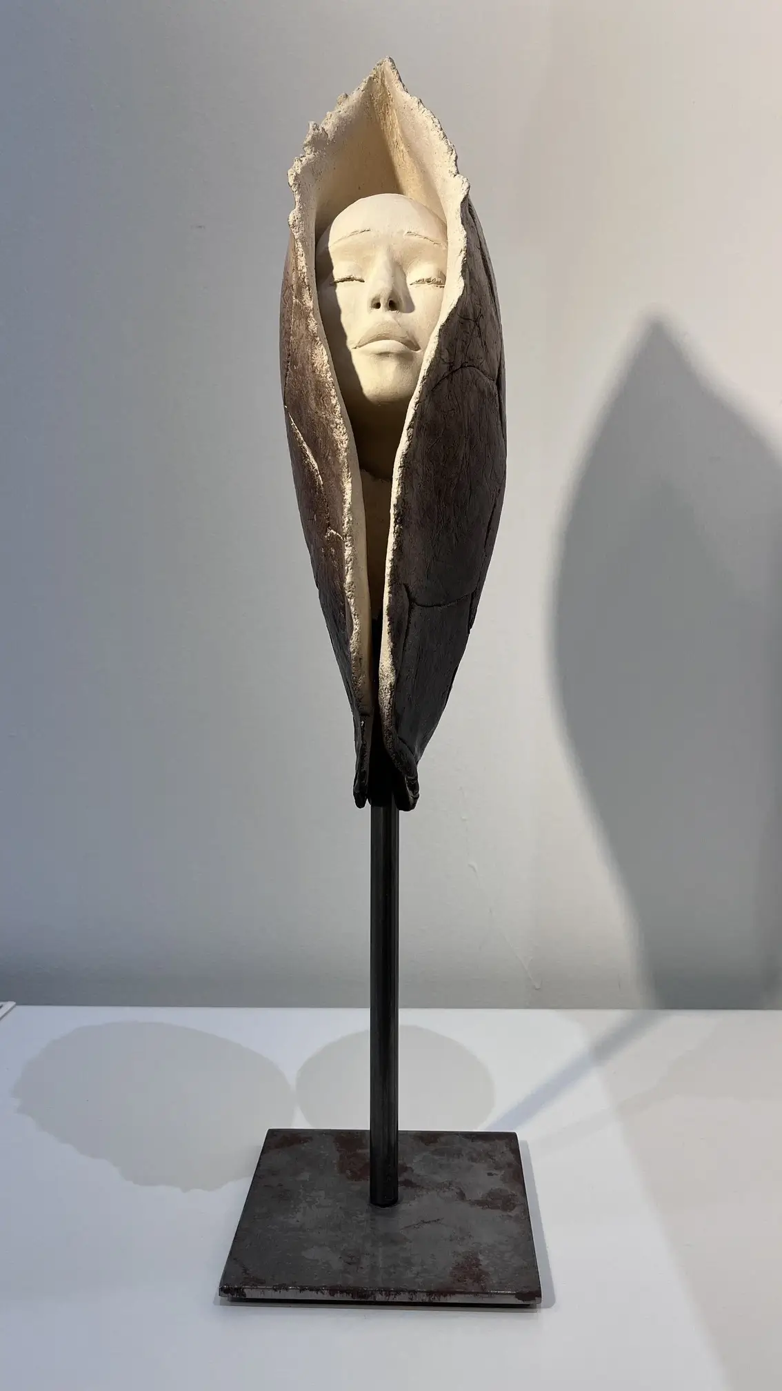 Sculpture en grès blanc représentant un visage serein émergeant d'une forme organique sur socle en métal noir minimaliste