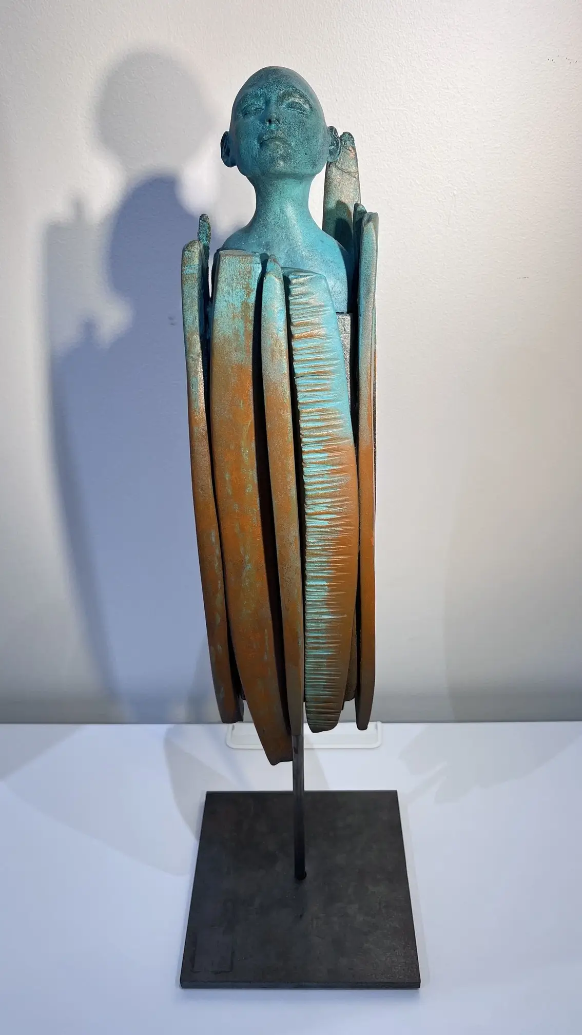 Sculpture en grès aux dégradés bleus et ocres, visage serein entouré de formes verticales incisées évoquant une protection.