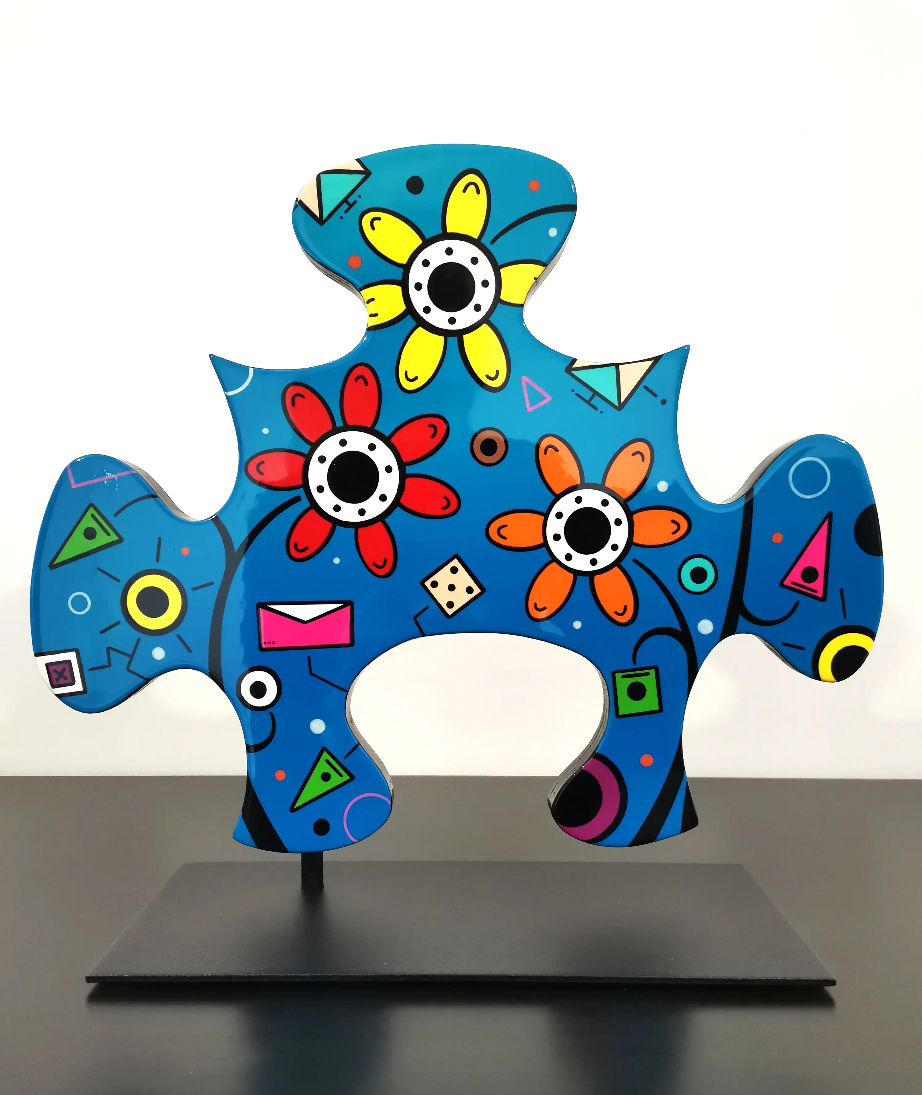 Sculpture puzzle bleue aux fleurs pop rouges et orange, motifs géométriques colorés et vernis brillant sur socle noir