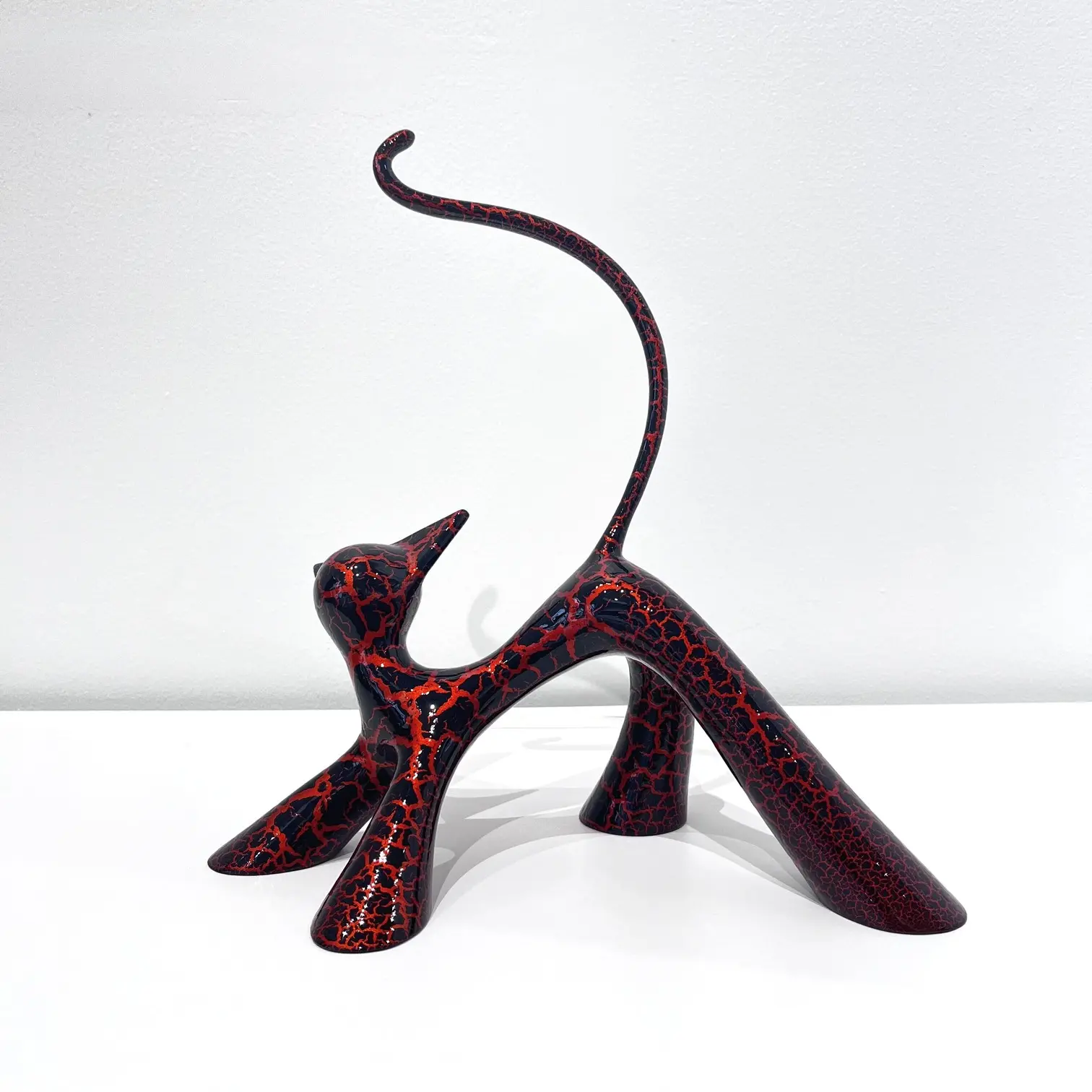 Chat sculptural orange craquelé, queue relevée, pattes écartées, finition brillante et textures fendillées.