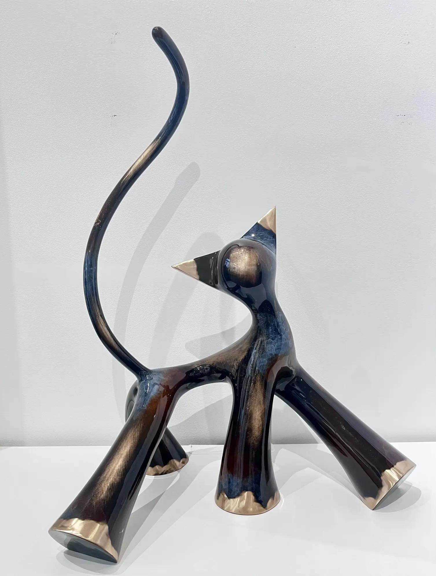 Sculpture monumentale noir marron gris meulé brossé, pattes massives, reflets chauds et froids mêlés.