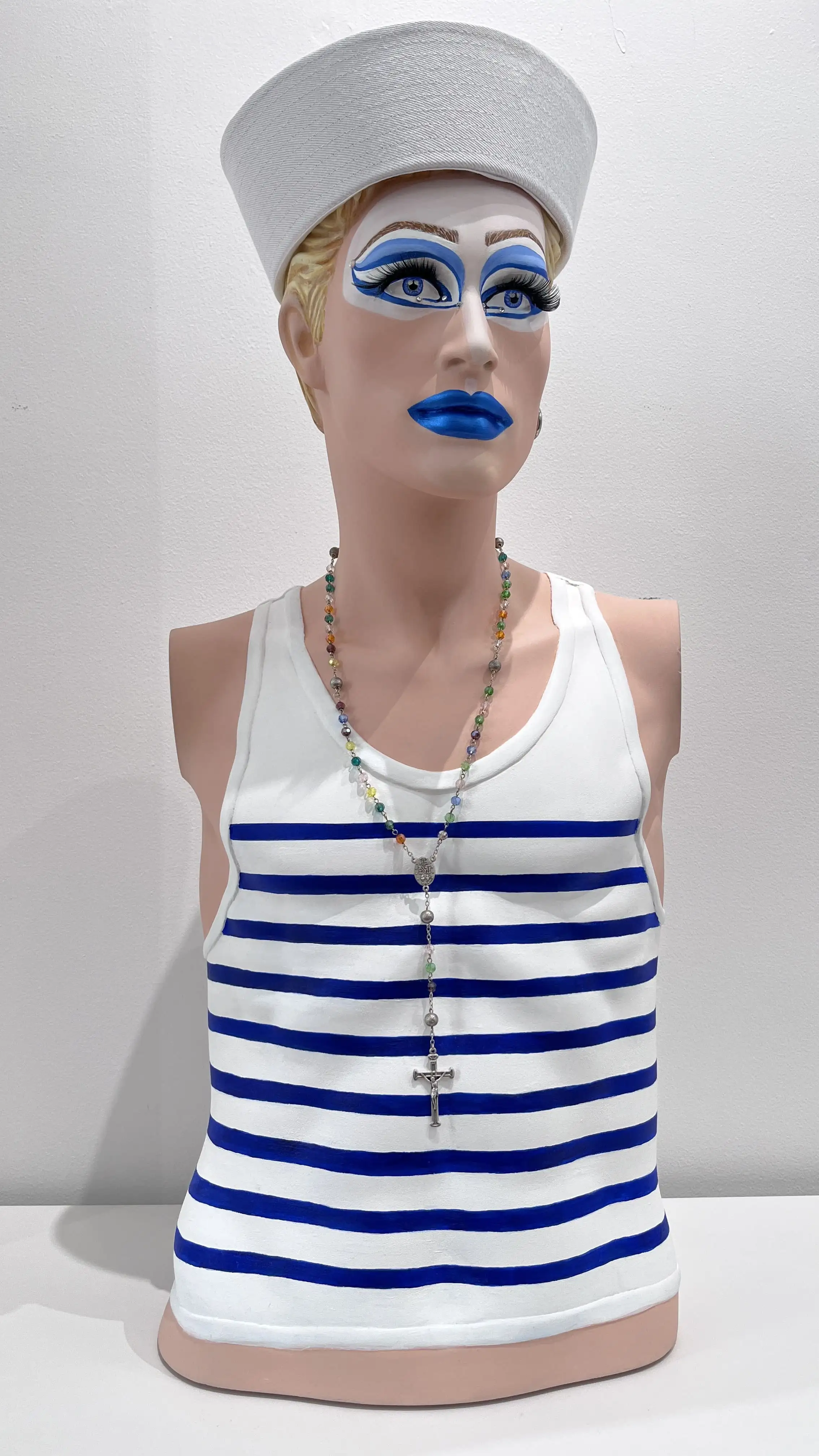 Buste de matelot au maquillage bleu graphique, marinière blanche et bleue, chapelet coloré, style pop art.