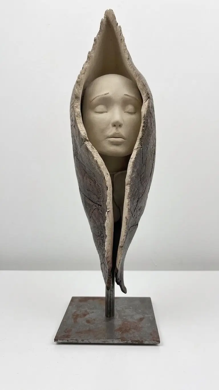 Sculpture en grès beige et gris sombre représentant un visage serein enveloppé dans une forme organique protectrice verticale. 