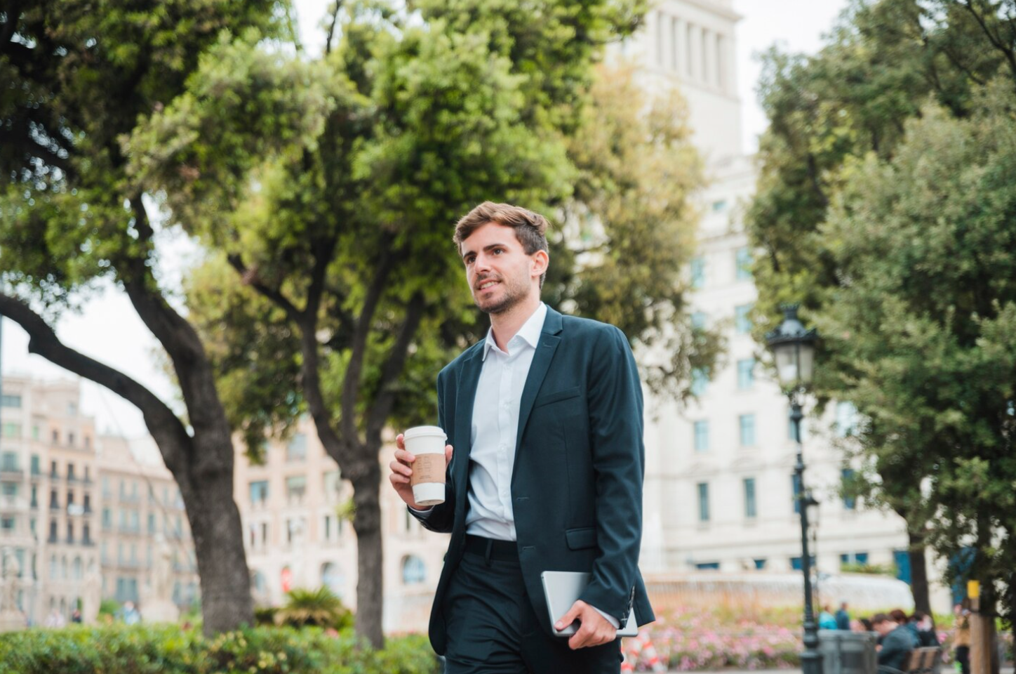 A professional man smilling and holding a cup of coffee while walking in the city