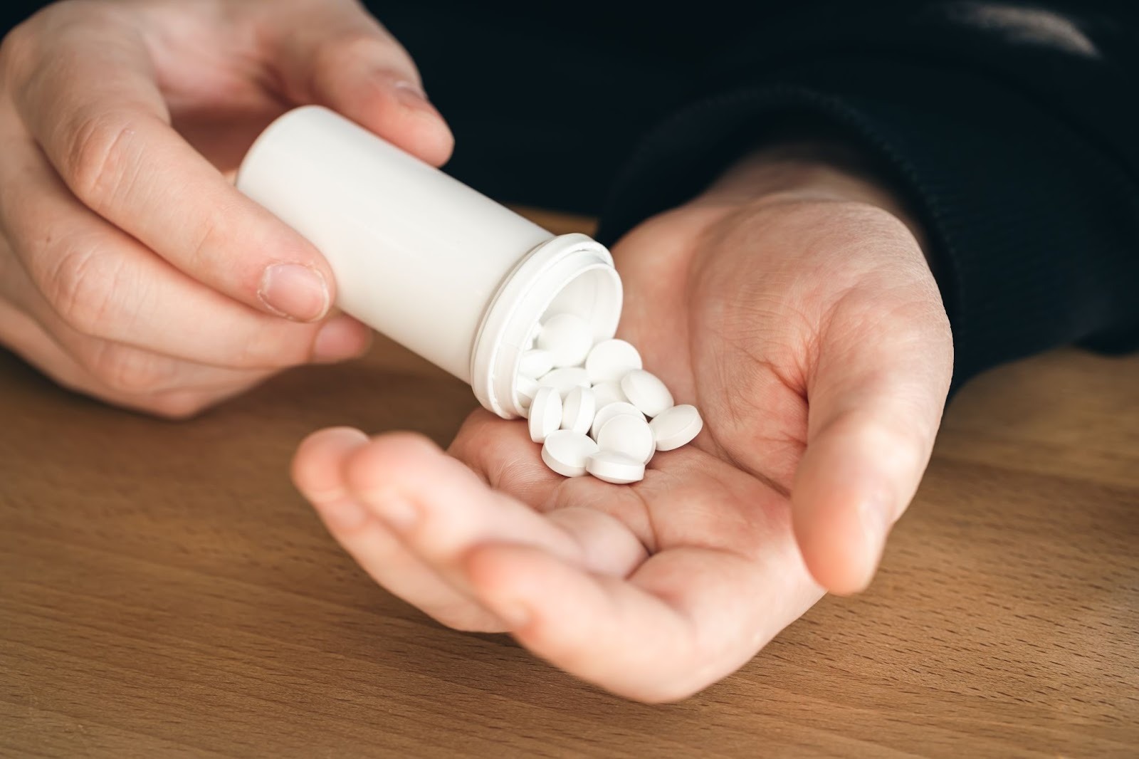 Hands pouring white tablets from a prescription bottle into an open palm over a wooden surface, representing medication management as part of meth addiction treatment