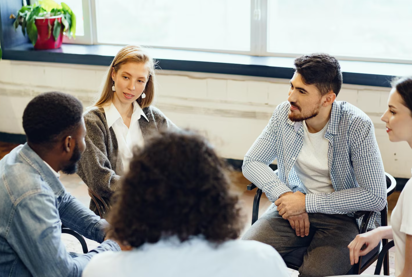A group of people sits in a circle during a therapy session, sharing experiences and support in addiction recovery