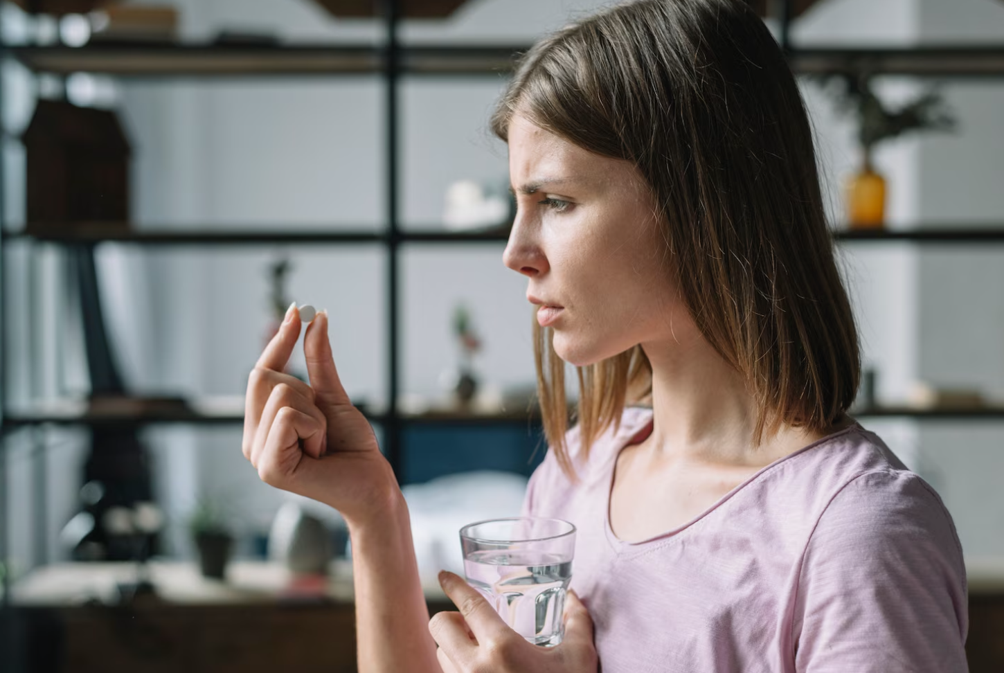 A woman examines a pill before taking it, reflecting the need to understand how medications can affect activities like driving