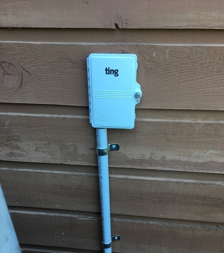 A photograph of a blue plastic NID box labeled 'Ting' attached to a house's side panelling on the outside of a home.