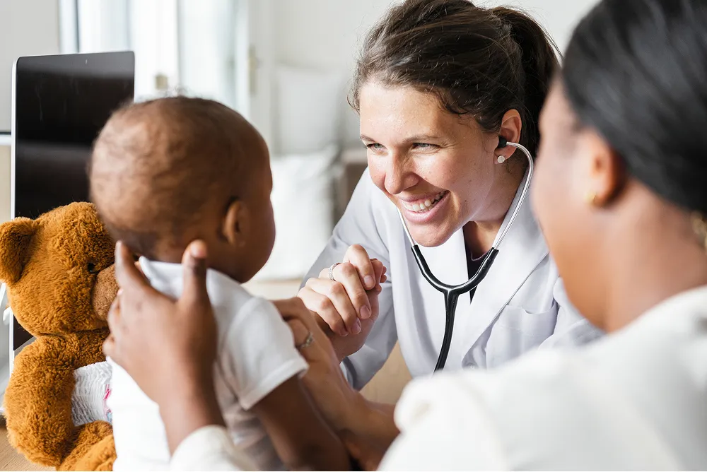 Female doctor smiling as she examines a happy baby held by by their mother.