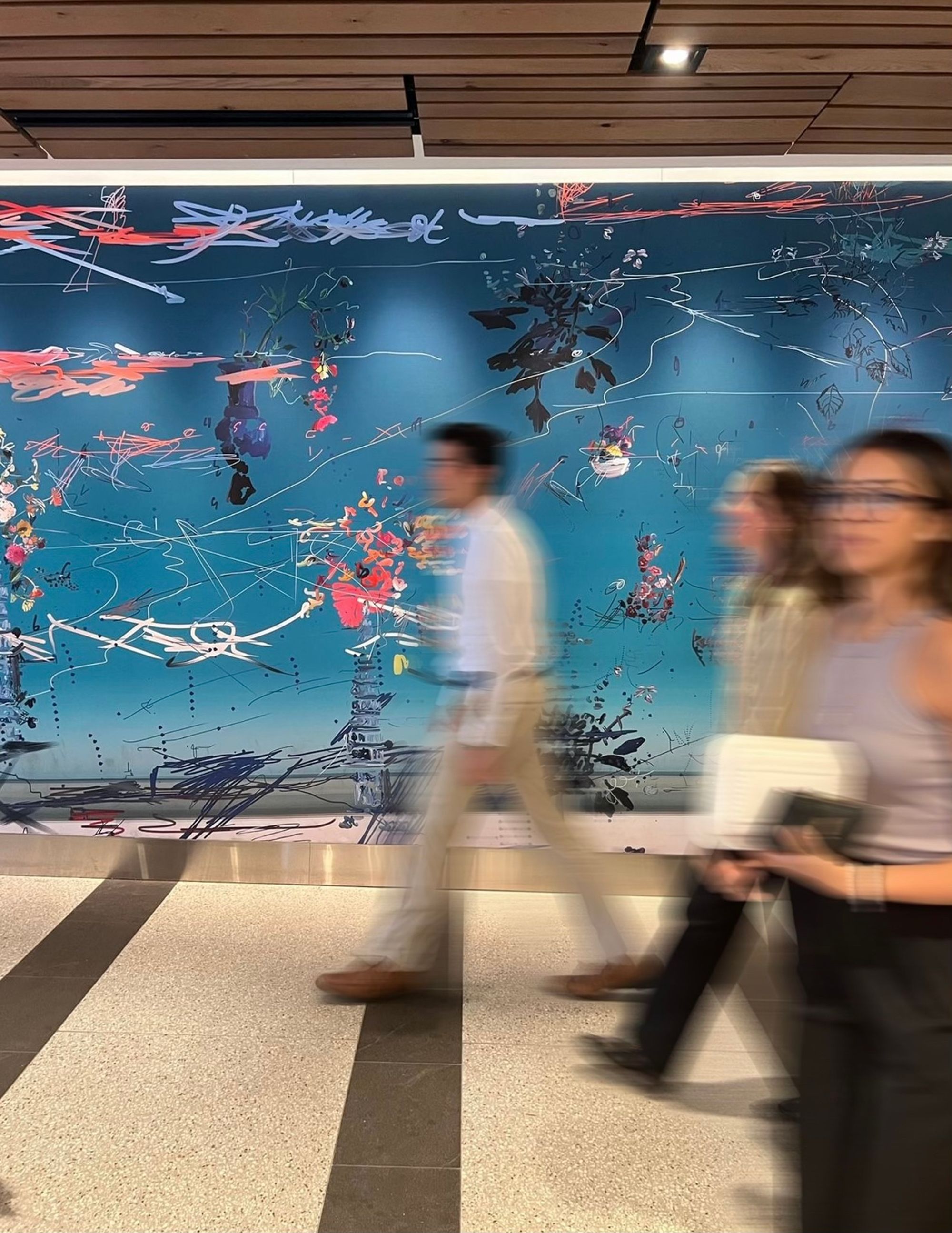 people walking past a large wall with a painting of flowers