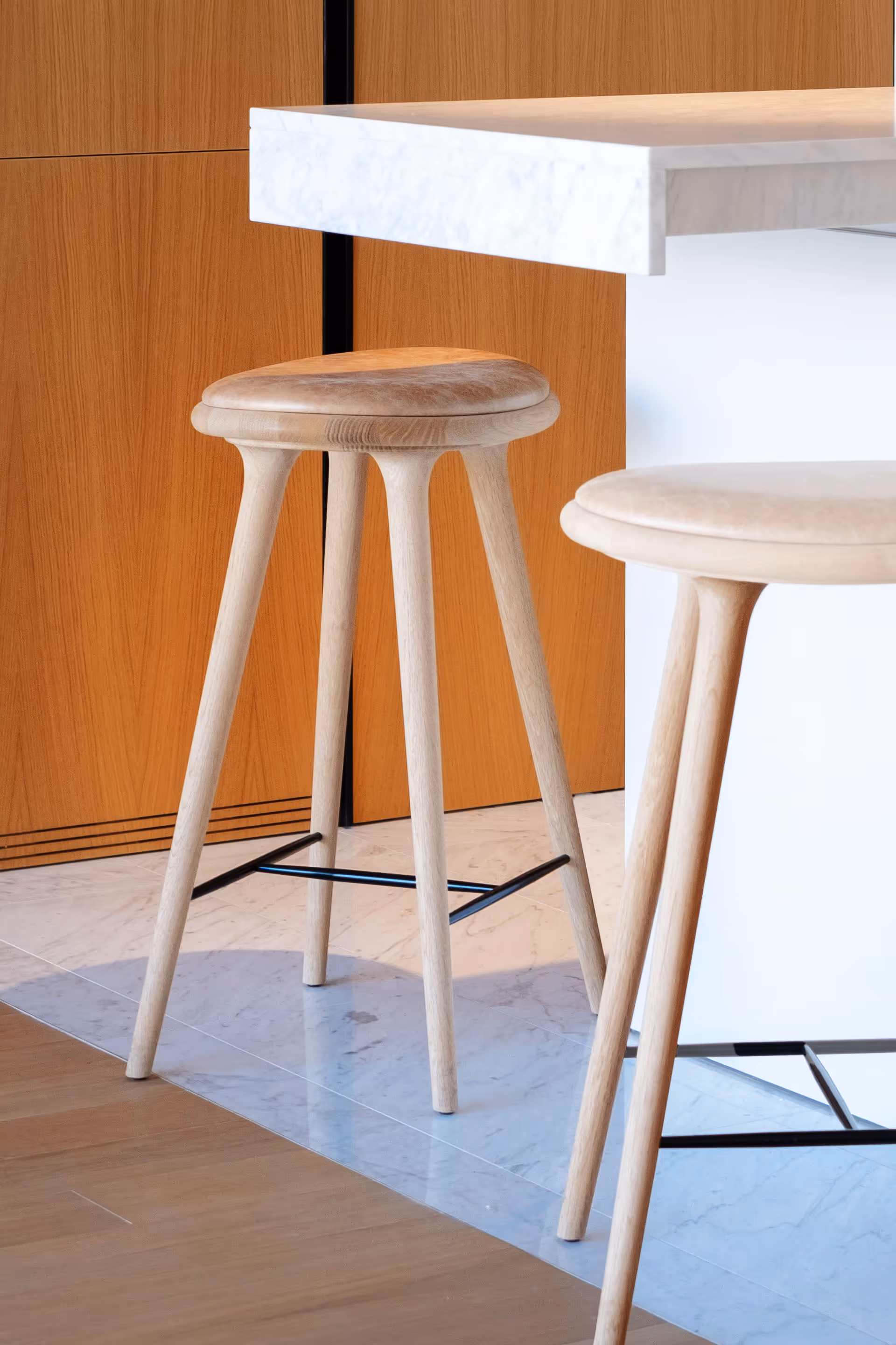 Detalle de taburetes de madera junto a encimera blanca en cocina moderna. Fotografía de interiores realizada por KC Studio en Barcelona.