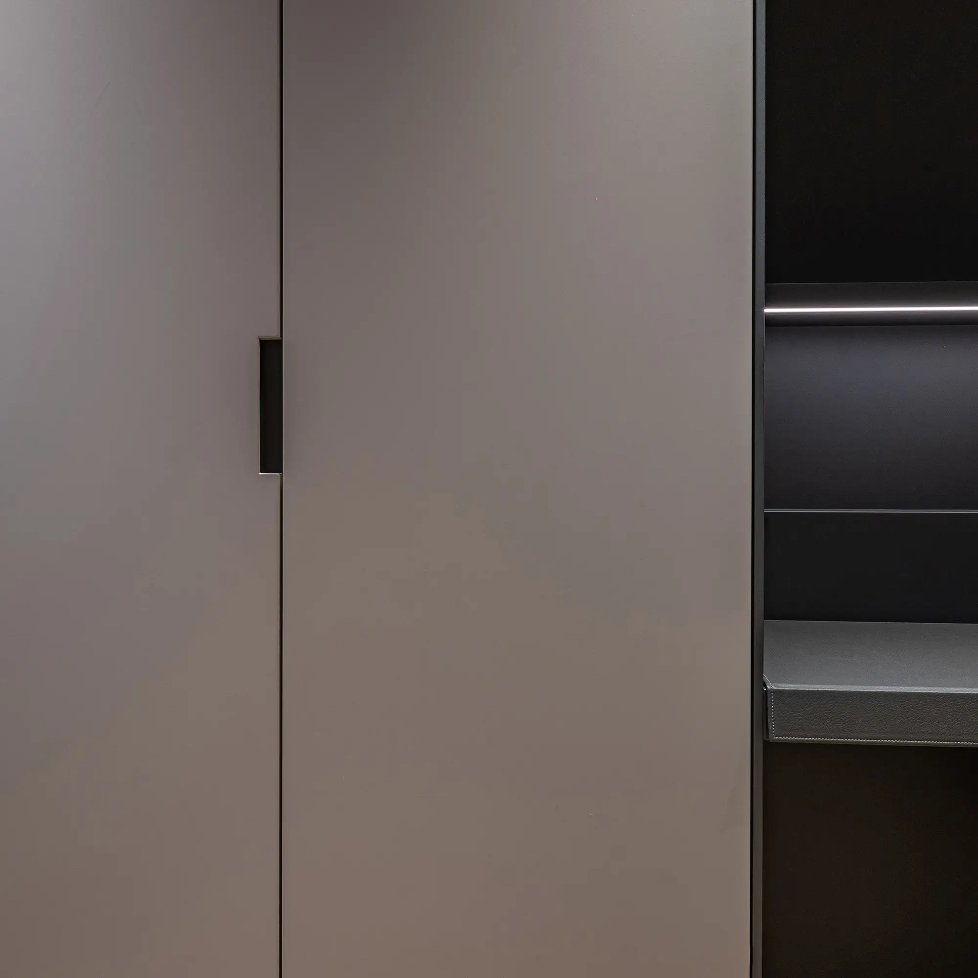 Esta imagen muestra un mueble de almacenamiento moderno y minimalista con una puerta en acabado gris mate y una sección de estantería abierta en negro en el lado derecho. El diseño elegante incluye un tirador empotrado, resaltando una estética limpia y funcional.