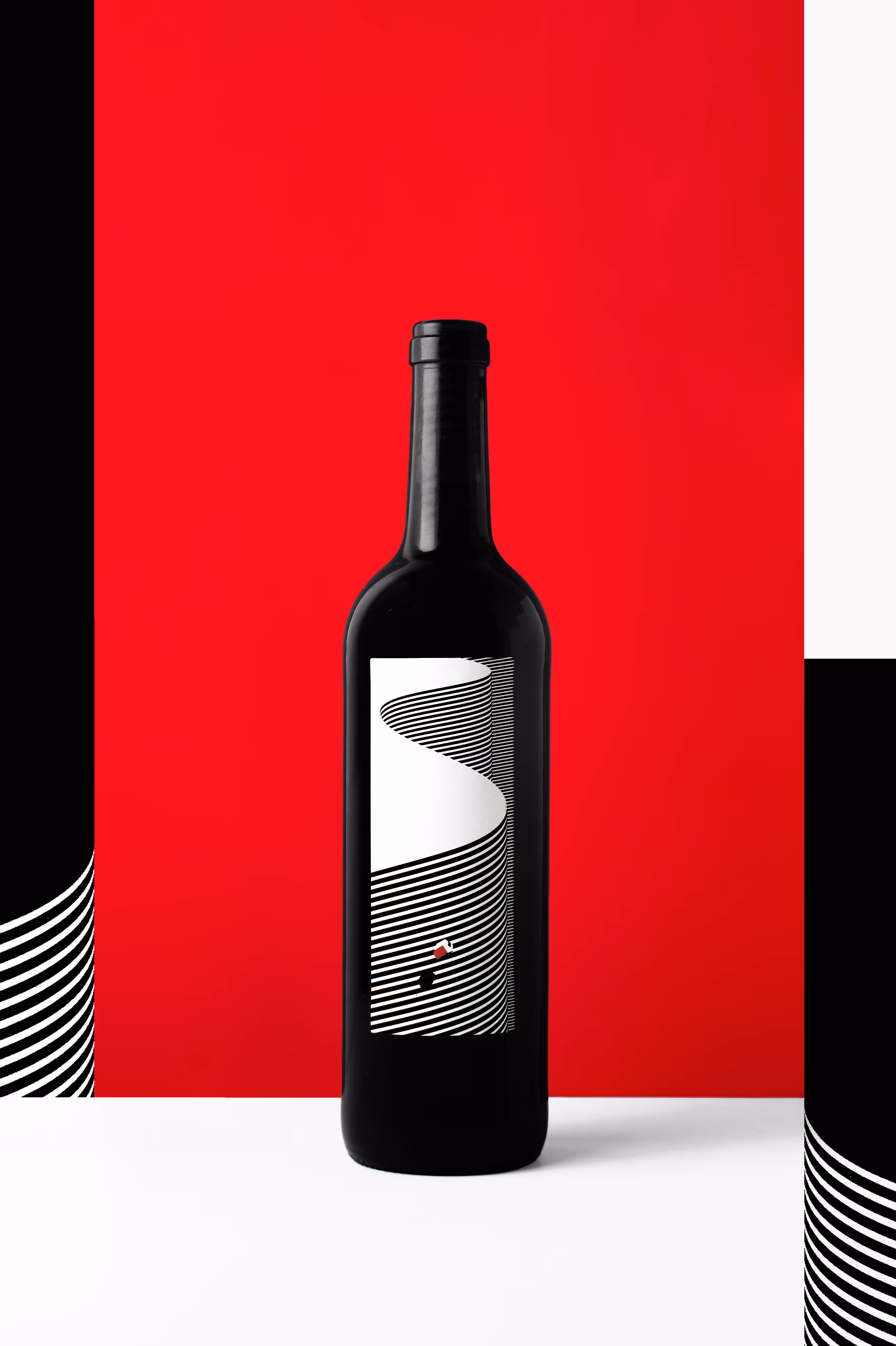 Una elegante botella de vino negra con una etiqueta minimalista que presenta atrevidas franjas curvas en blanco y negro formando un camino, todo sobre un fondo rojo vibrante. El diseño es llamativo y moderno, creando un fuerte contraste visual entre los elementos rojos y negros.