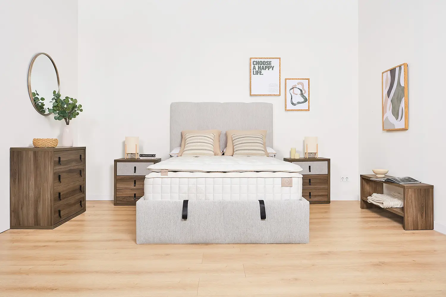 Detalle de cama tapizada en tejido beige claro con colchón de muelles ensacado de alta gama, acompañado de una mesita de noche de madera con cajones combinados en tela y tiradores negros. Decoración en tonos neutros y estilo moderno.