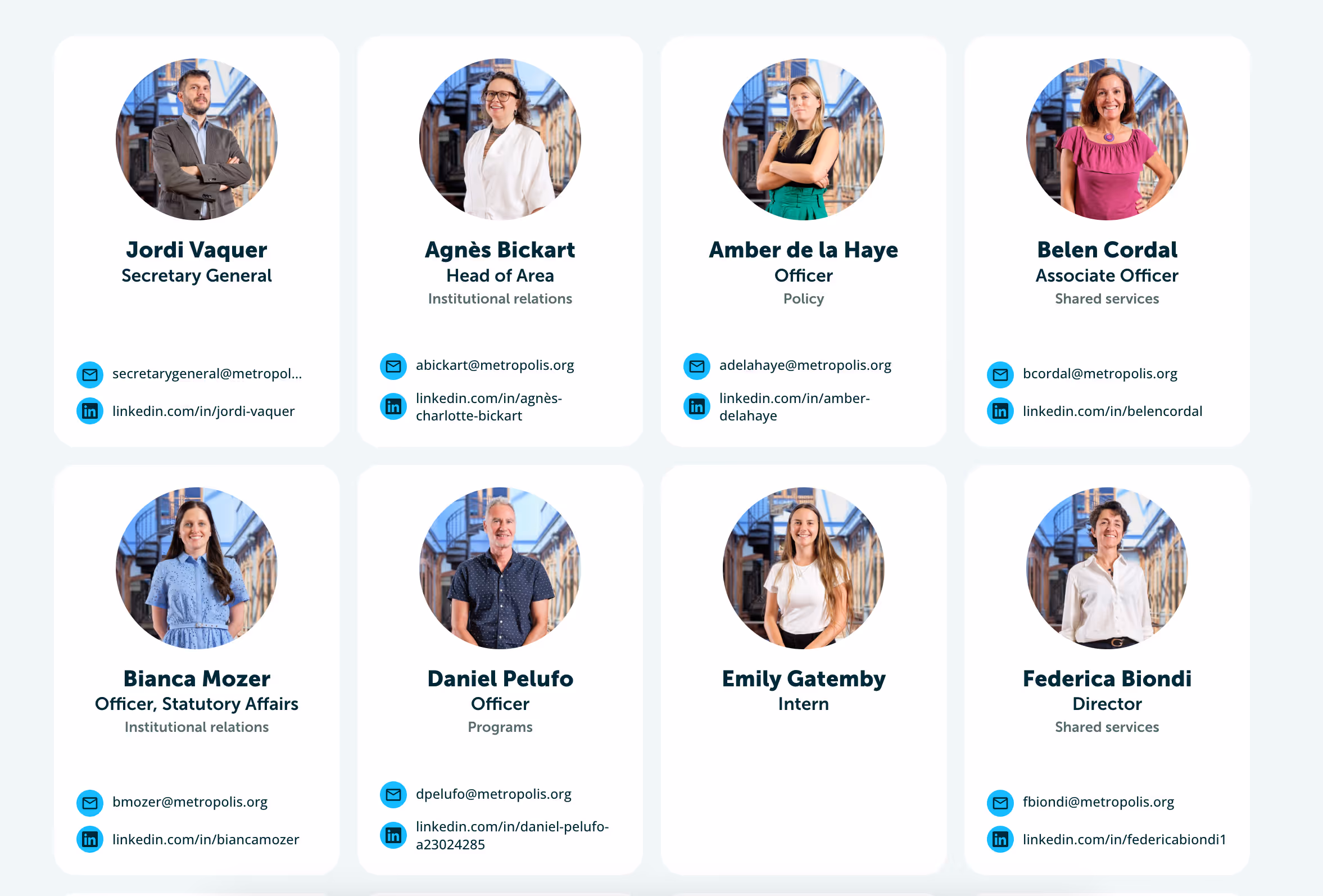 Foto en blanco y negro de una persona sonriente apoyada contra una pared, vistiendo una camiseta "be.komorebi". Un letrero iluminado arriba dice "I FEEL GOOD," y ventanas de vidrio texturizado enmarcan parte del fondo, creando una atmósfera relajada y alegre.