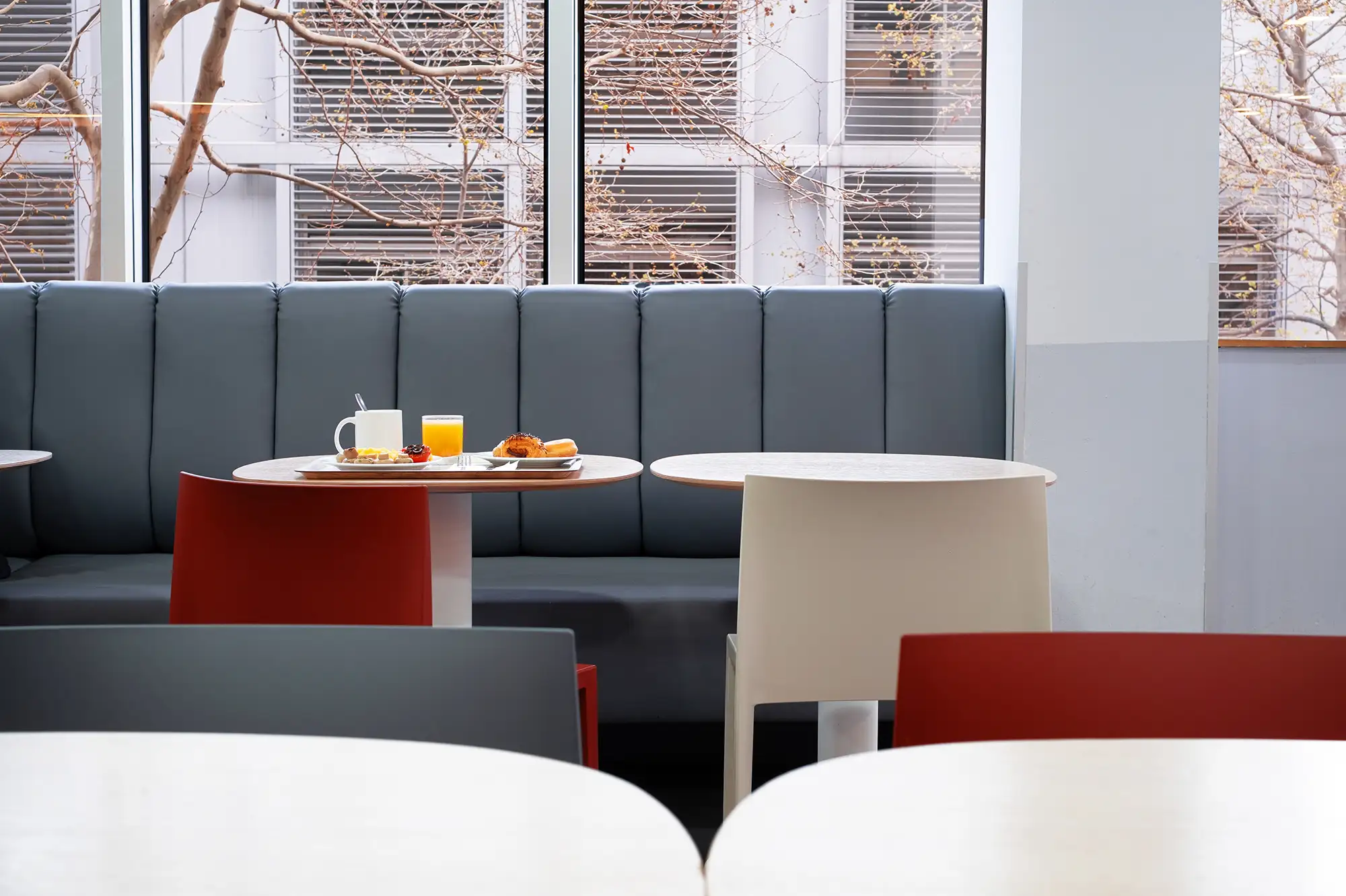 Interior moderno de cafetería de hotel en Barcelona con mesas minimalistas, bancos acolchados y desayuno servido junto a una ventana con luz natural.