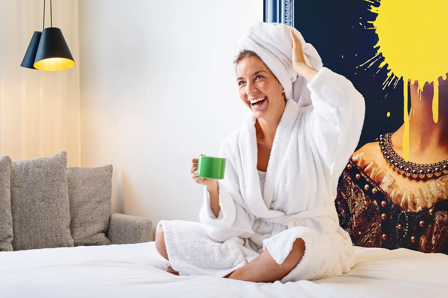 clienta del hotel sentada en su cama sonriendo y bebiendo su cafe