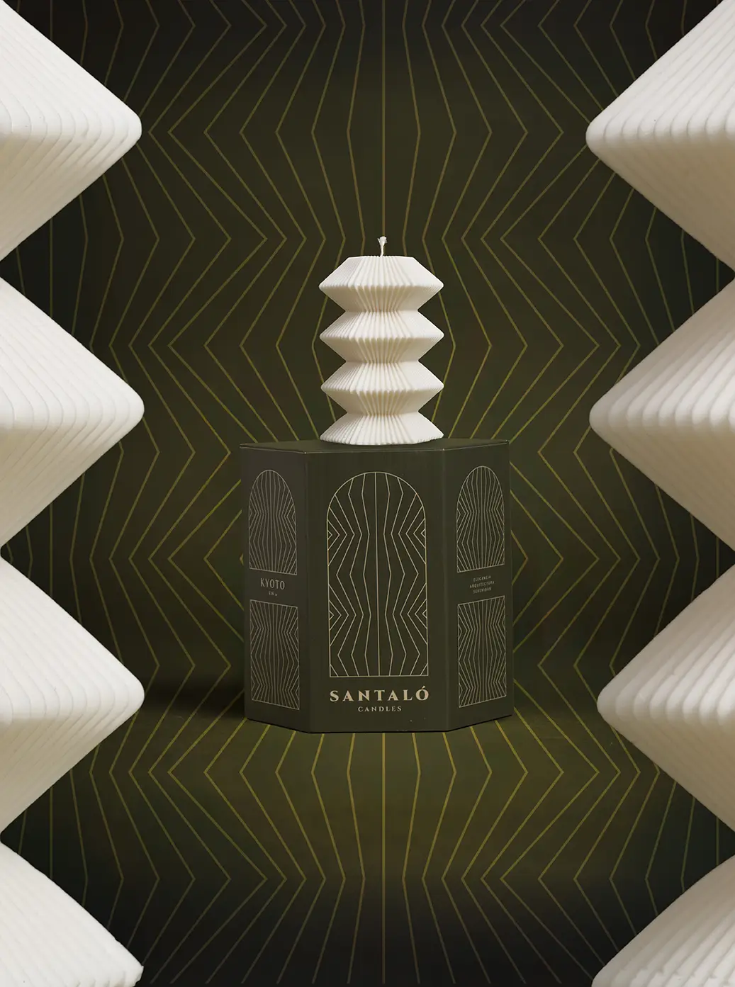 Vela geométrica blanca sobre base verde oscuro, con fondo simétrico en relieve, iluminación lateral suave.
