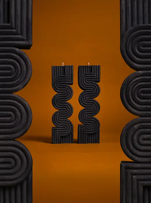 Velas negras de diseño geométrico sobre fondo naranja intenso, enmarcadas por estructura ondulada