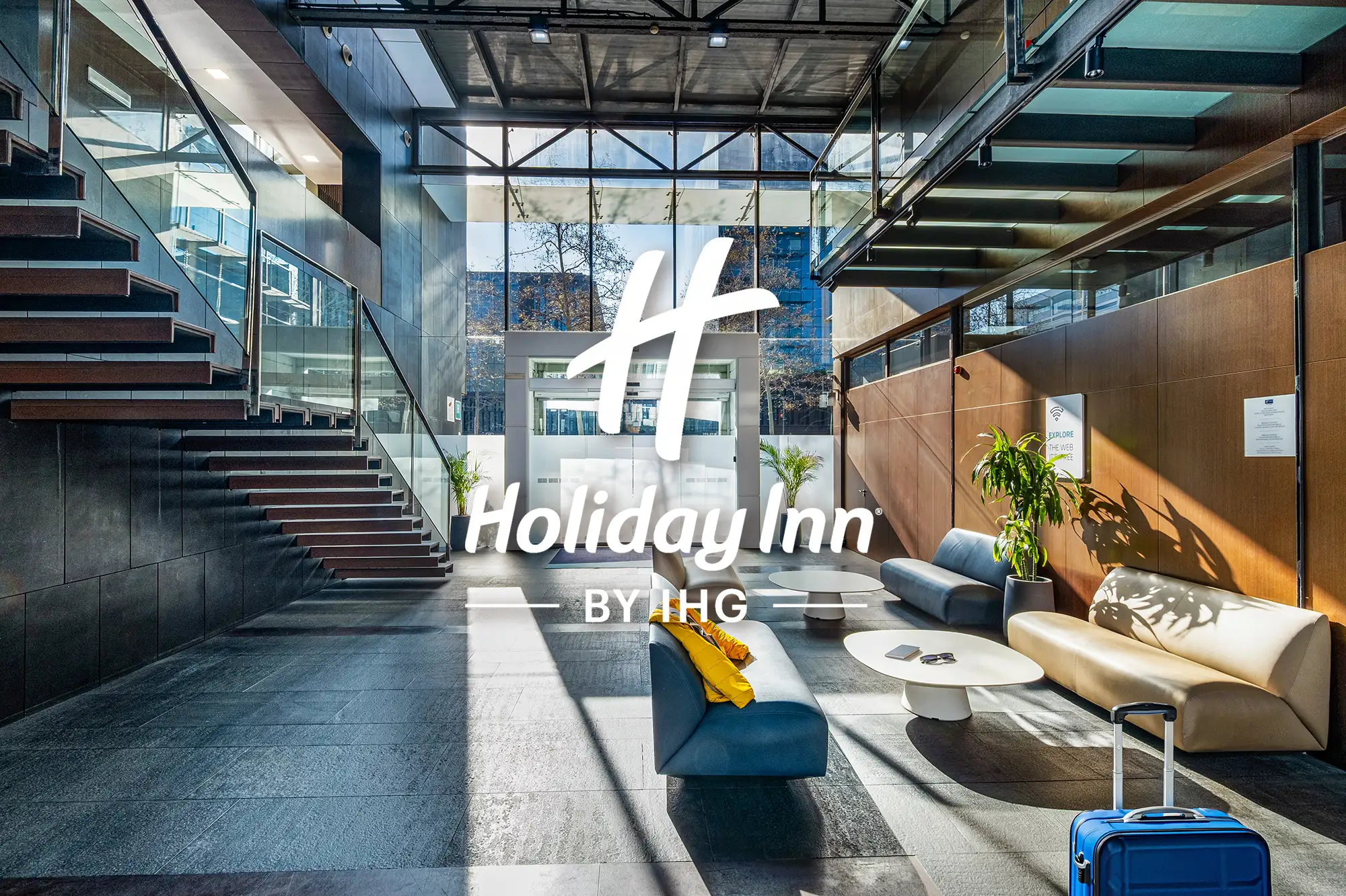 Lobby moderno del hotel Holiday Inn Express Barcelona con luz natural, escaleras abiertas y zona de descanso contemporánea