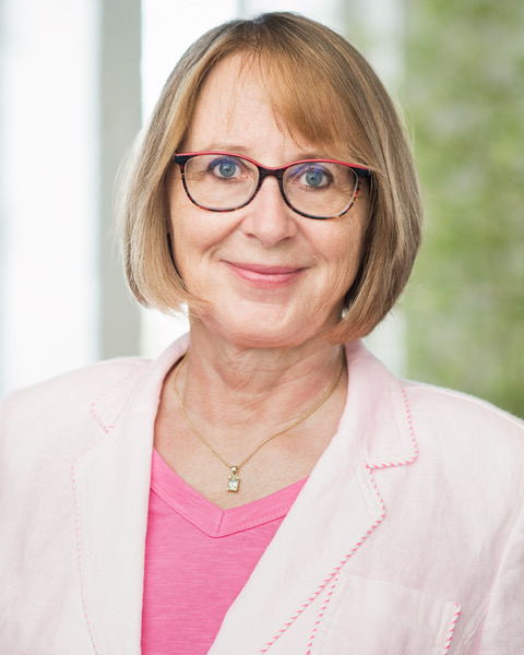 A 65 year old woman with glasses and a doctors robe.