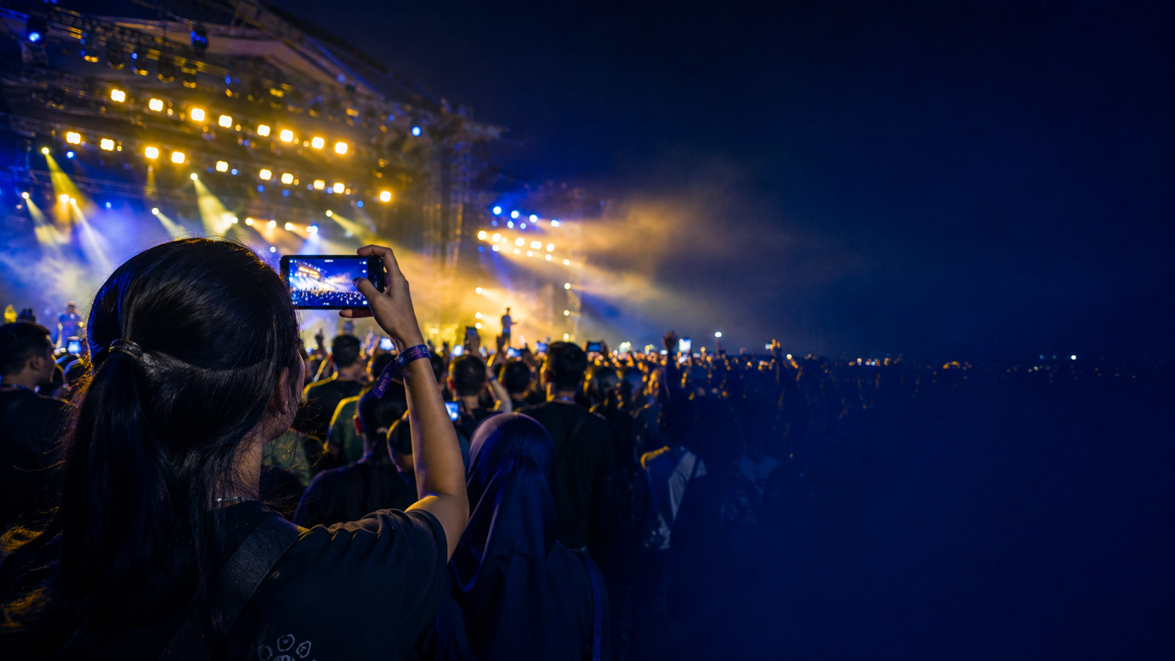 Concert crowd filming a live performance under blue stage lights