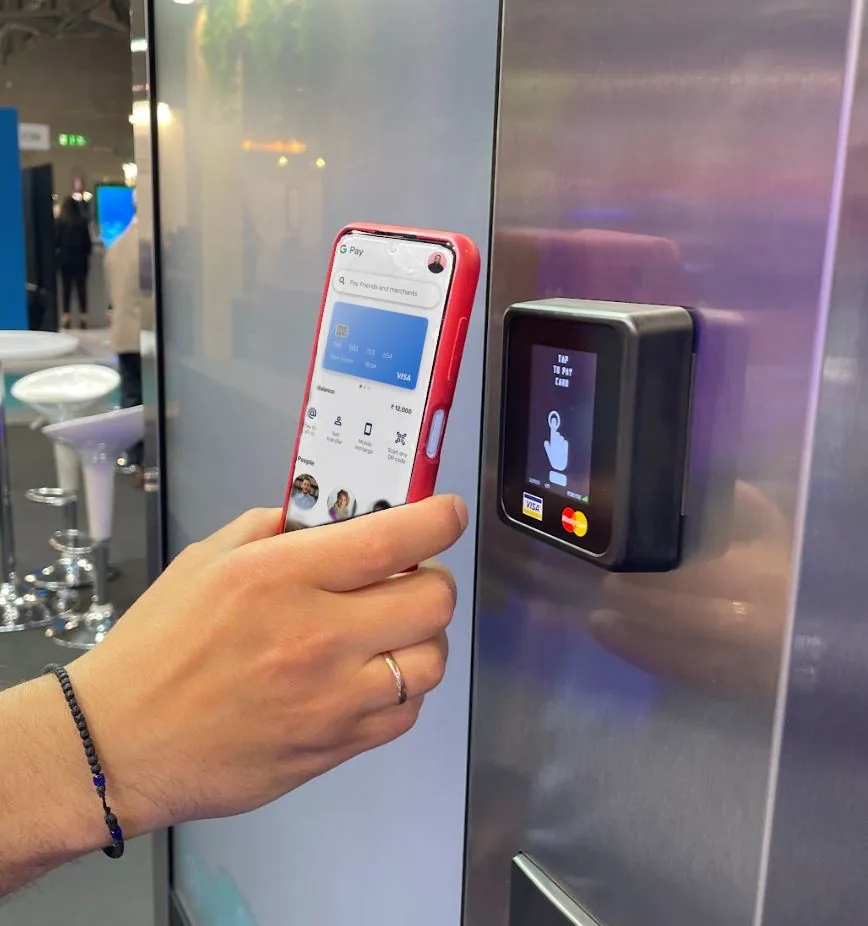 A guest taps a phone with Google Pay on an Aurency reader mounted on a machine
