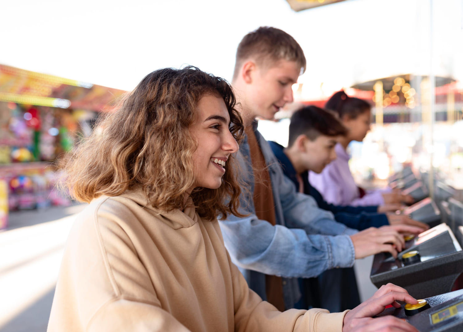 Teenagers playing arcade machines side by side at a family entertainment centre, smiling and having fun