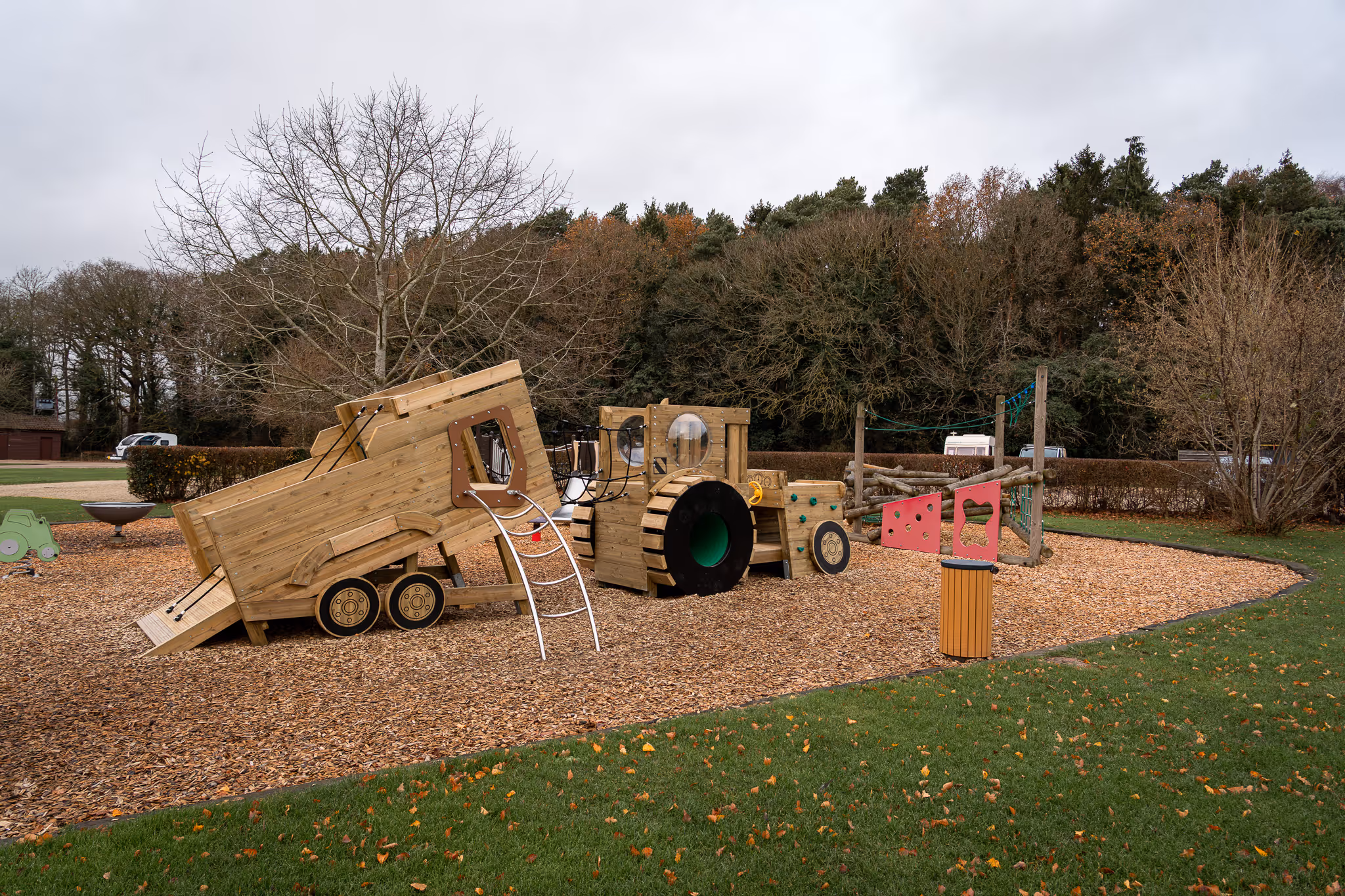 Wooden playground structure shaped like a tractor with slides and climbing features on a wood chip surface.