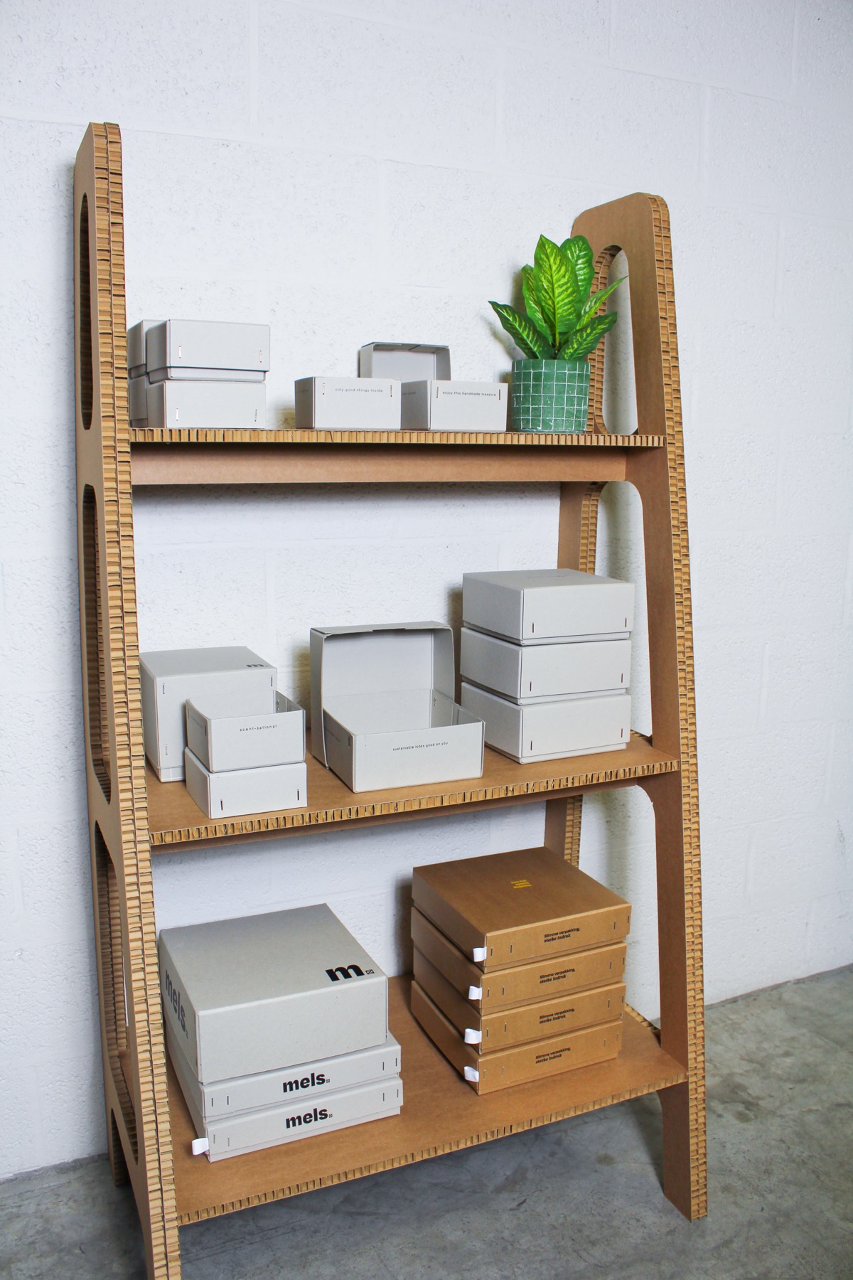 Three-tiered shelving unit made of corrugated cardboard displaying various cardboard boxes and packaging materials in a studio setting