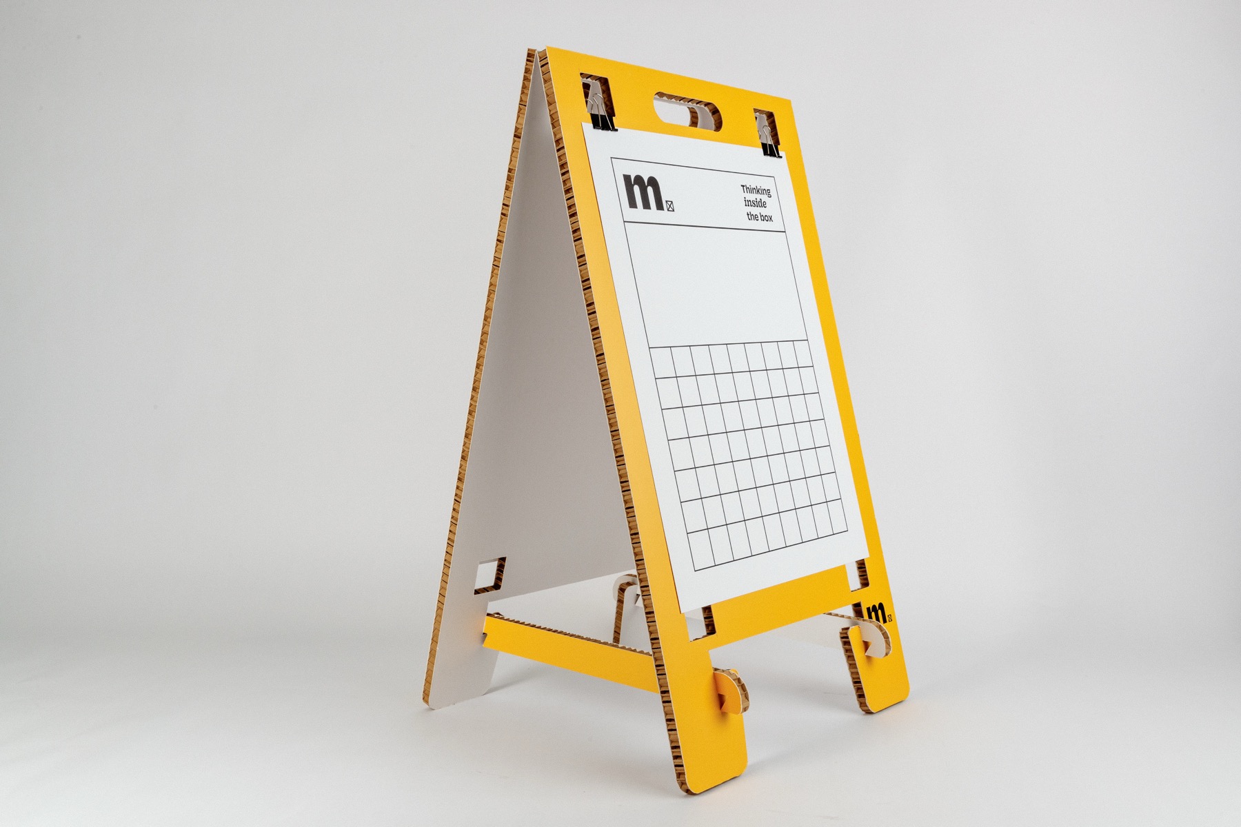 Yellow A-frame display stand made from corrugated cardboard with white paper attached, featuring mels branding and grid pattern
