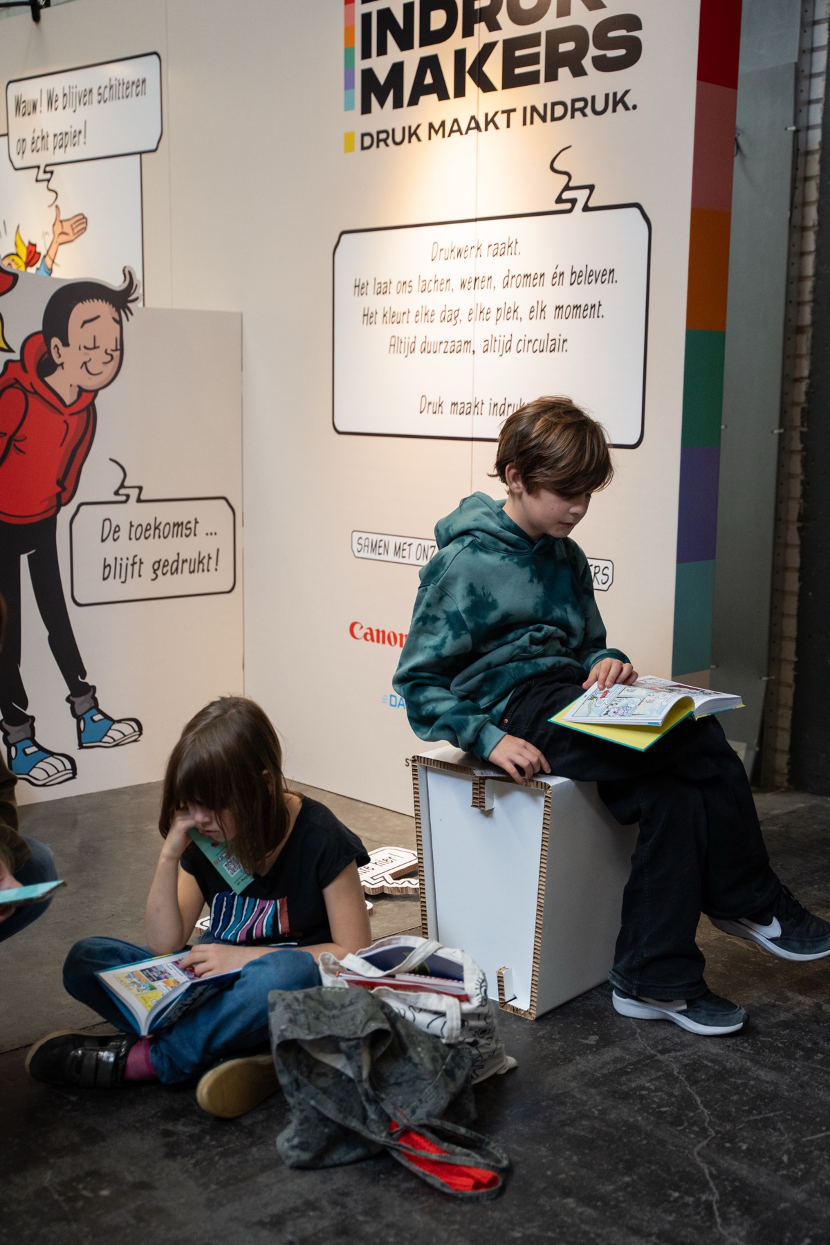 Two children reading books at a print media exhibition, surrounded by colorful wall graphics promoting the impact of print