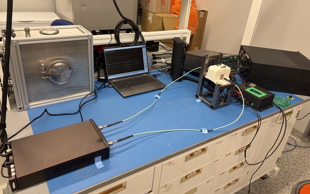 Dielectric measurement bench: a vector network analyzer connected by RF cables to a sample fixture, with a laptop showing the readout