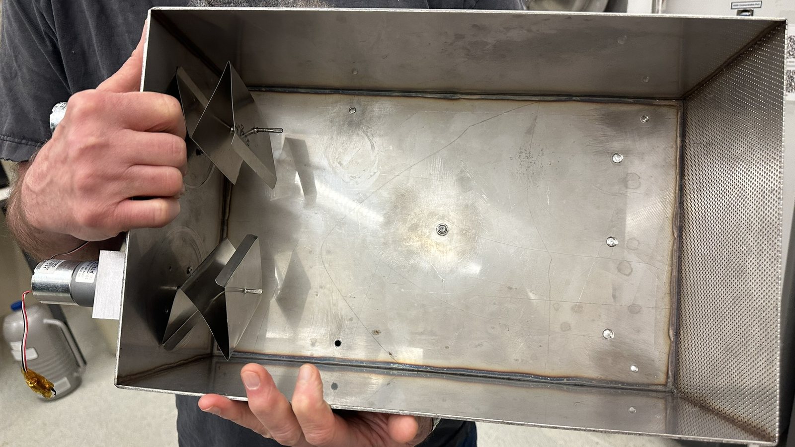 The original shoebox-sized microwave heating prototype: a stainless steel box with perforated walls and a small motor